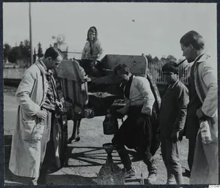 Men and children at a cart in a street, one man crouching over a wine demijohn, Nicosia.