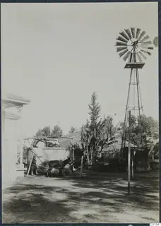 Yard in Nicosia with a windmill, a donkey and a person beside a stone water tank