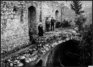 Four people standing and sitting among stone ruins with pointed arched openings and trees, in the Kyrenia Mountains