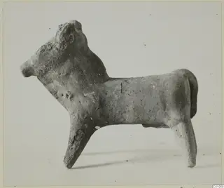 Terracotta figurine of a standing bull facing left, shown in side profile against a pale background