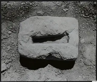 Rectangular pale stone block with a rectangular hollow in its top, lying on loose soil at Tomb 422, Lapithos Kastros