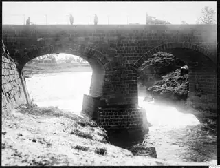 Arched masonry bridge over water at Nicosia, with four people on the deck above the arches.