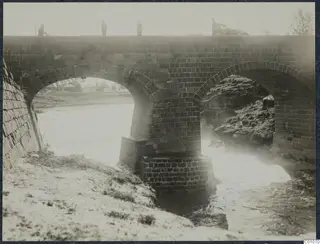 Two-arched stone bridge over a stream bed, with four people on the deck above, at Nicosia.