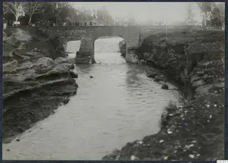 River flowing under a brick arched bridge at Nicosia, with people standing along the bridge rail