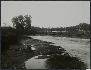 River channel with sandy banks, stony debris and a line of trees along the far bank.