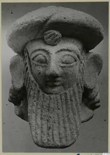 Terracotta Neo-Cypriote head with a flat cap, large ears and a long vertically ribbed beard, front view.