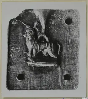 Flat rectangular stone with a relief carving of a head in profile and three pierced holes.