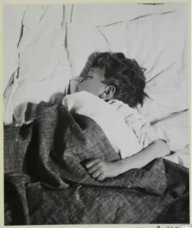 Sleeping child lying on a white pillow under a grey blanket.