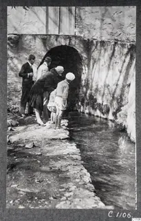 Visitors looking down at a stream beside a stone wall with an arched opening, Kythrea