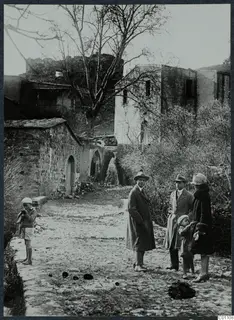 Street in Kythrea with stone buildings, a bare tree and five people standing on the cobbled lane