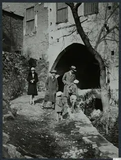 Two men, a woman and two children walk on a stony path past a vaulted archway in a stone building at Kythrea.