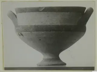 Pottery White Painted I bowl with two short side handles and a tall flared foot, seen in side view against a plain background.