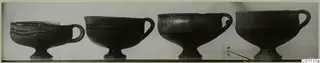 Four footed bowls with single loop handles standing in a row, photographed from the side.