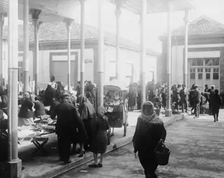 Market square in Nicosia with people at stalls and a crowd under a long colonnade of columns.