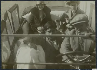 Two passengers, a child and a driver inside an open car, photographed through the windscreen frame.