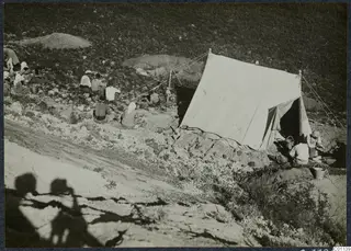 People sitting near a large white tent with baskets and buckets on a slope at Marion