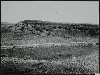 Hillside at Sikarka-Kokkina, Marion, with a row of dark tomb openings cut into its face and one small standing figure at left