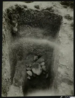 Tomb 5 at Marion during excavation, with a pile of stones and a vessel set in the trench wall.