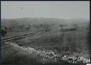 Landscape at Soli with a stone wall in the foreground, a dirt track and rolling hills behind