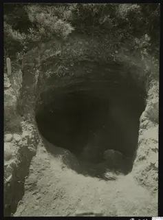 Excavated Tomb 13 at Marion: a dark opening cut into pale earth, with grass above and stones at the edges