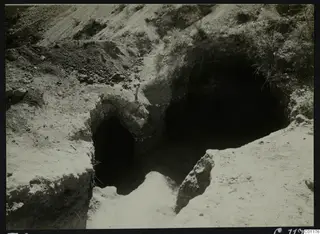Excavated tomb entrances cut into a sandy slope at Marion, with a dark chamber opening beyond.