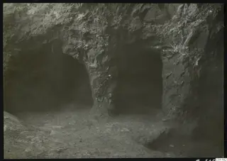 Tomb 9 at Marion: two dark arched openings cut into a rock face, with an earthen floor in front