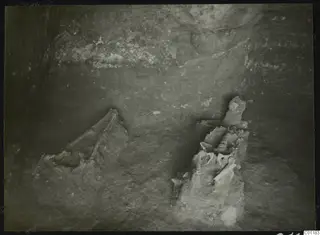 Tomb 9 at Marion during excavation, with a skeleton lying among stones in a rock-cut chamber