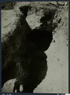 Excavation of Tomb 23 at Marion, with a dark opening cut into pale soil and grass along the top edge.