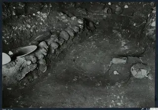 Excavation view at Marion showing pottery vessels in situ beside a row of stones in the soil