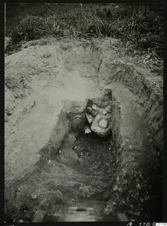 Excavated pit at Marion with a dromos-like cutting, grass above and a cluster of stones at the far end