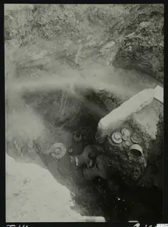 Tomb 14 at Marion during excavation, with pottery vessels and a large stone slab lying in the pit