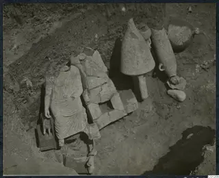 Tomb 30 at Marion: a headless draped stone statue and large stone vessels among stone fragments during excavation