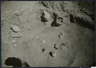 Excavated tomb floor at Marion with scattered pottery vessels, lids and small objects in situ.