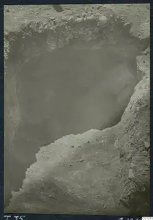Excavation of Tomb 35 at Marion, with a dark cavity in the cut and stones along the upper edge.
