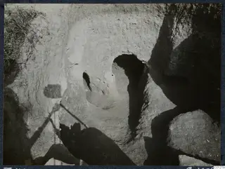 Rock-cut tomb opening with a rounded doorway in an excavated earth bank at Marion