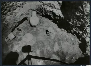 Tomb 45 at Marion during excavation, with pottery vessels and stones on the floor of a rock-cut chamber