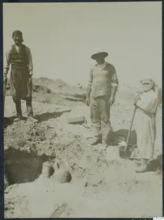 Three people standing in an excavation at Marion, with pottery vessels partly uncovered in the trench in front of them.