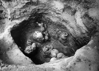 Tomb 47 at Marion, interior, with pottery vessels lying and standing among rock blocks in an excavated pit