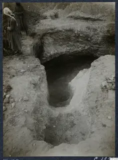 Tomb 38 at Marion during excavation, with a woman holding a tool beside an open cut leading to a dark tomb opening