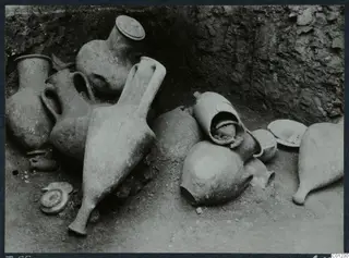 Pottery vessels lying in situ on the floor of Tomb 55 at Marion, against a rough rock-cut wall