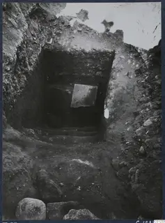 Tomb 53 at Marion during excavation, with steps leading up to a square stone slab in the back wall.