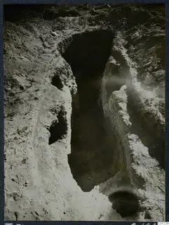 Excavation of Tomb 31 at Marion: a deep cut in pale soil with a dark opening in one wall and loose stones beside it.