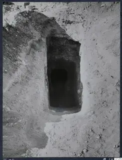 Tomb 39 at Marion: a sloping dromos leading down to the dark doorway of a tomb chamber in excavated ground.