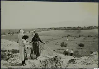 Women working at the edge of an excavation trench at Marion, one holding a rope above a bucket.