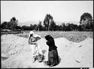 Two women with headscarves draw water from a pit at Marion, using buckets on ropes.