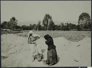 Two women with buckets working on a spoil heap at Marion, fields and trees behind them.
