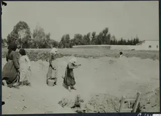 Women in headscarves and long skirts working in a sandy excavation trench at Marion, with a ladder at the edge.