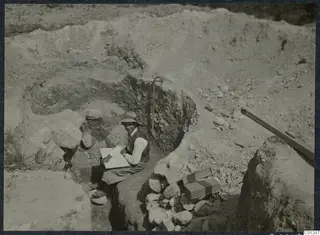 Erik Sjöqvist sitting in an excavated cut at Marion, writing or drawing in an open notebook on his knee