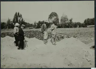 Four men stand and walk over a spoil heap at the Marion excavation, with fields and trees behind them.