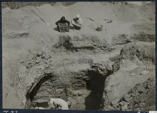 Excavation of Tomb 37 at Marion, with workers seated at the cut edge and a rope and bucket going down into the trench.